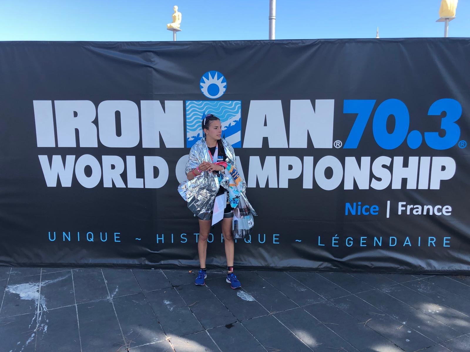 Fátima Alanís wrapped in the silver finisher's thermal blanket in front of the official Ironman 70.3 World Championship backdrop in Nice, France 2019.